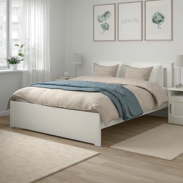 Классическая двуспальная кровать белого цвета в светлом интерьере спальни.